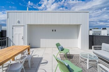 A patio with green chairs and a wooden table and a white building